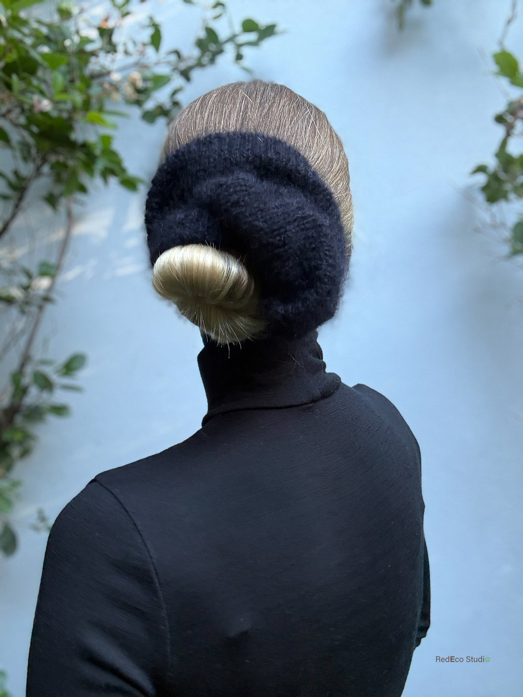 Person wearing a dark scrunchie with a textured pattern against a light blue wall.