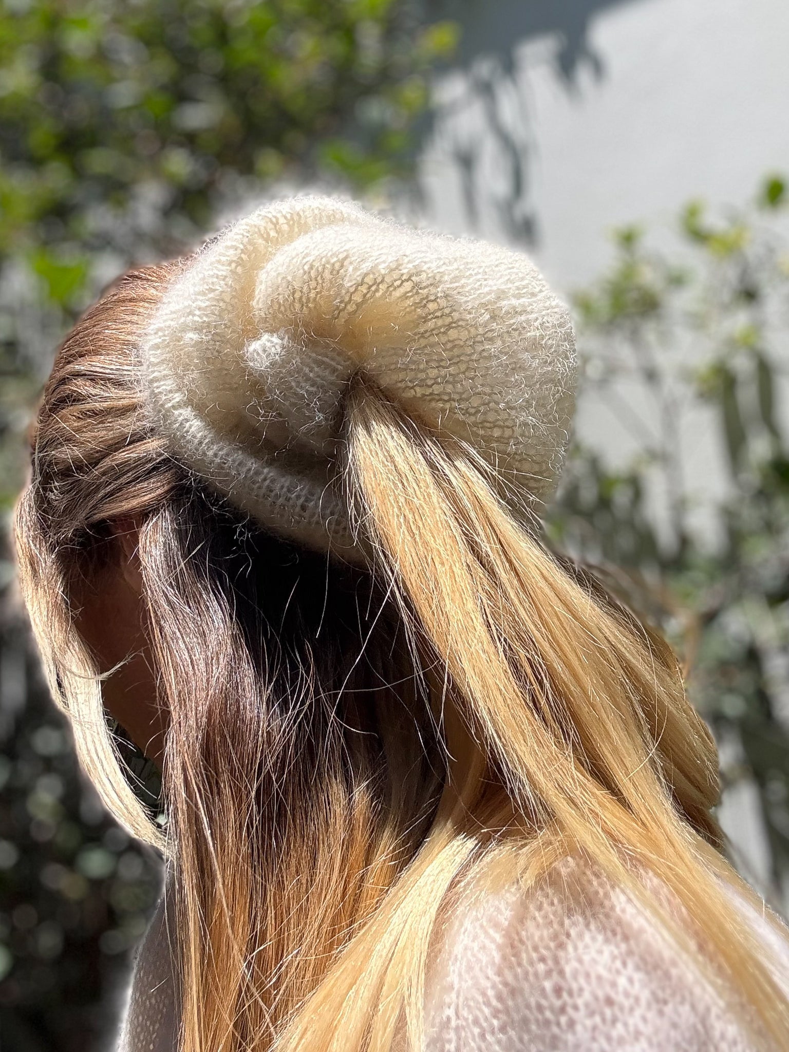Close-up of a large knitted cream hair scrunchie with a blurred natural background.