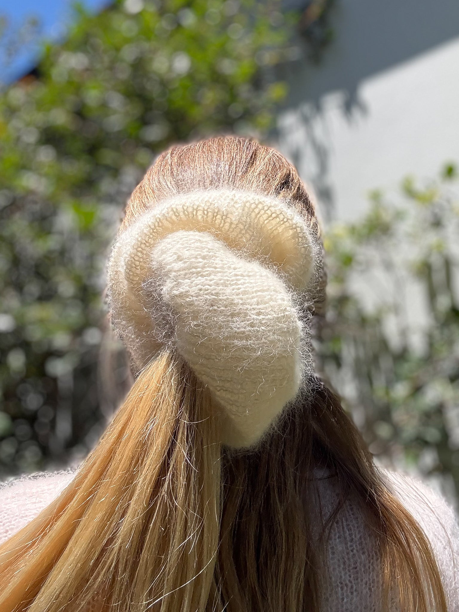 Person with a white hair scrunchie in their ponytail against a blurred outdoor background