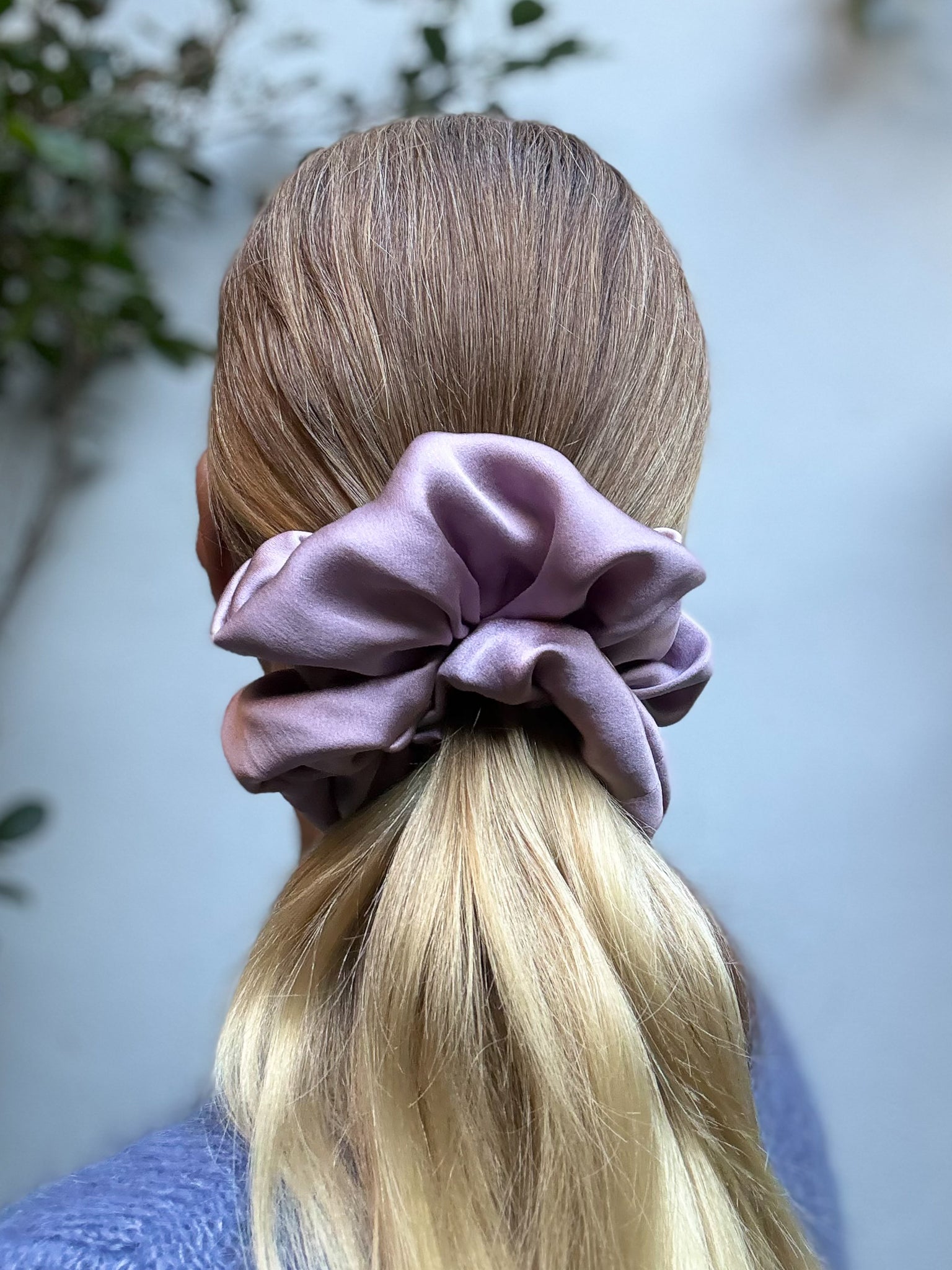 Person with a purple scrunchie in their hair against a blurred natural background