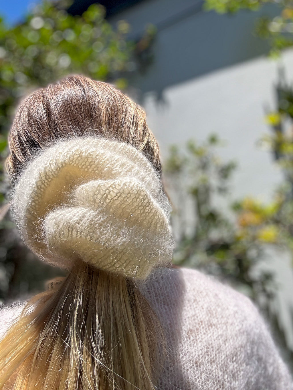 Close-up of a beige scrunchie on a ponytail with blurred outdoor background