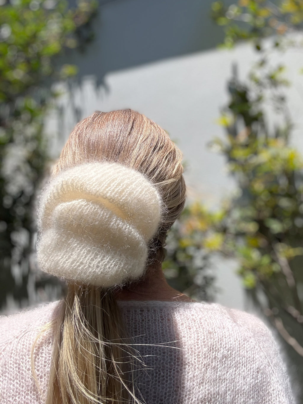 Person wearing a white knitted scrunchie with a blurred outdoor background