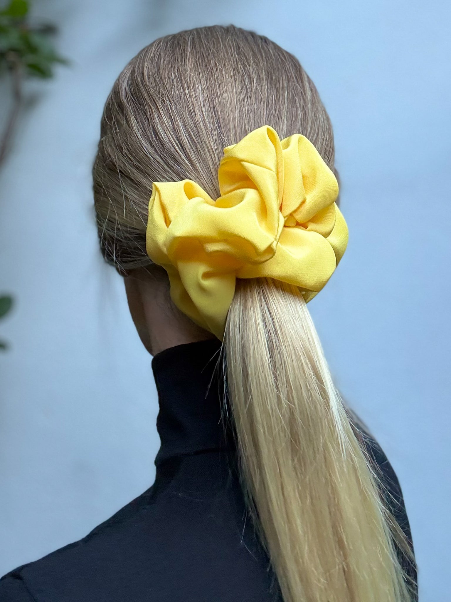 Person with a yellow scrunchie in their hair against a blurred natural background