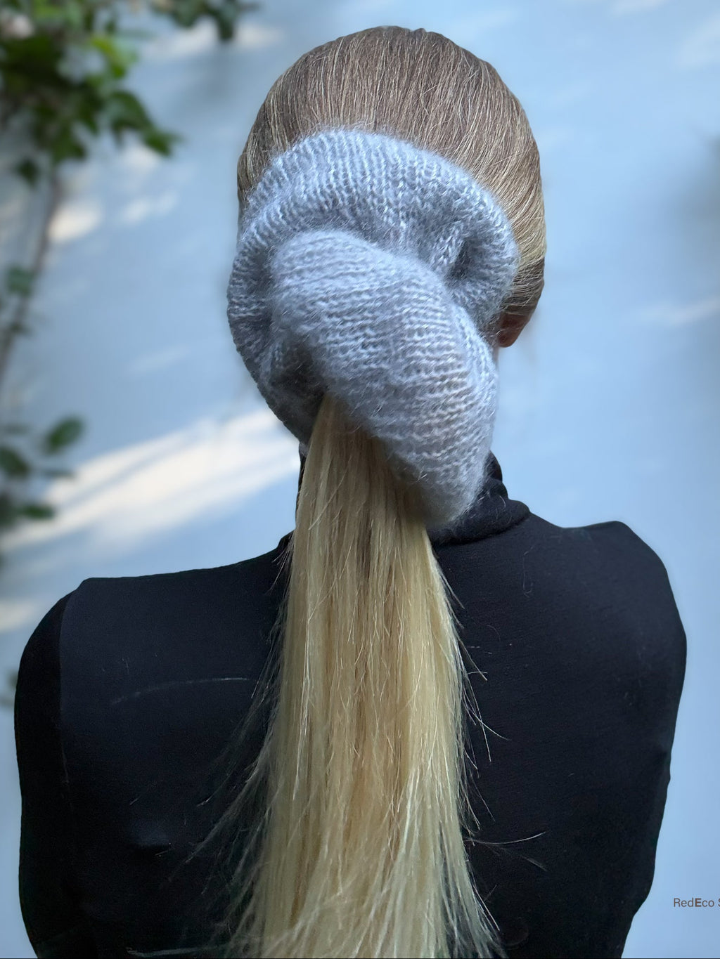 Person wearing a xl hand-knitted gray  scrunchie with a long blonde ponytail, standing against a light background.