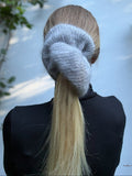 Person wearing a xl hand-knitted gray  scrunchie with a long blonde ponytail, standing against a light background.