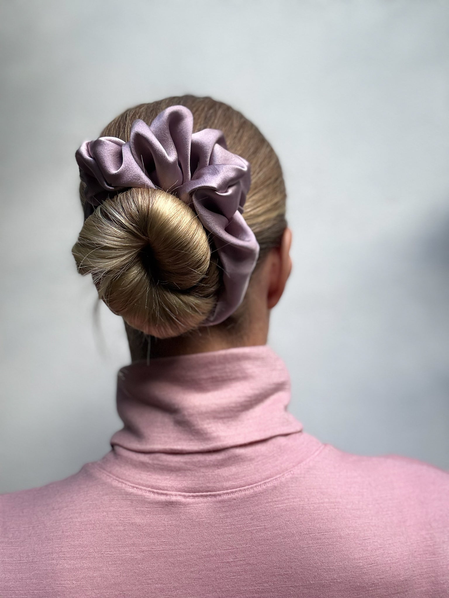 Person wearing a pink scrunchie in their hair against a plain background