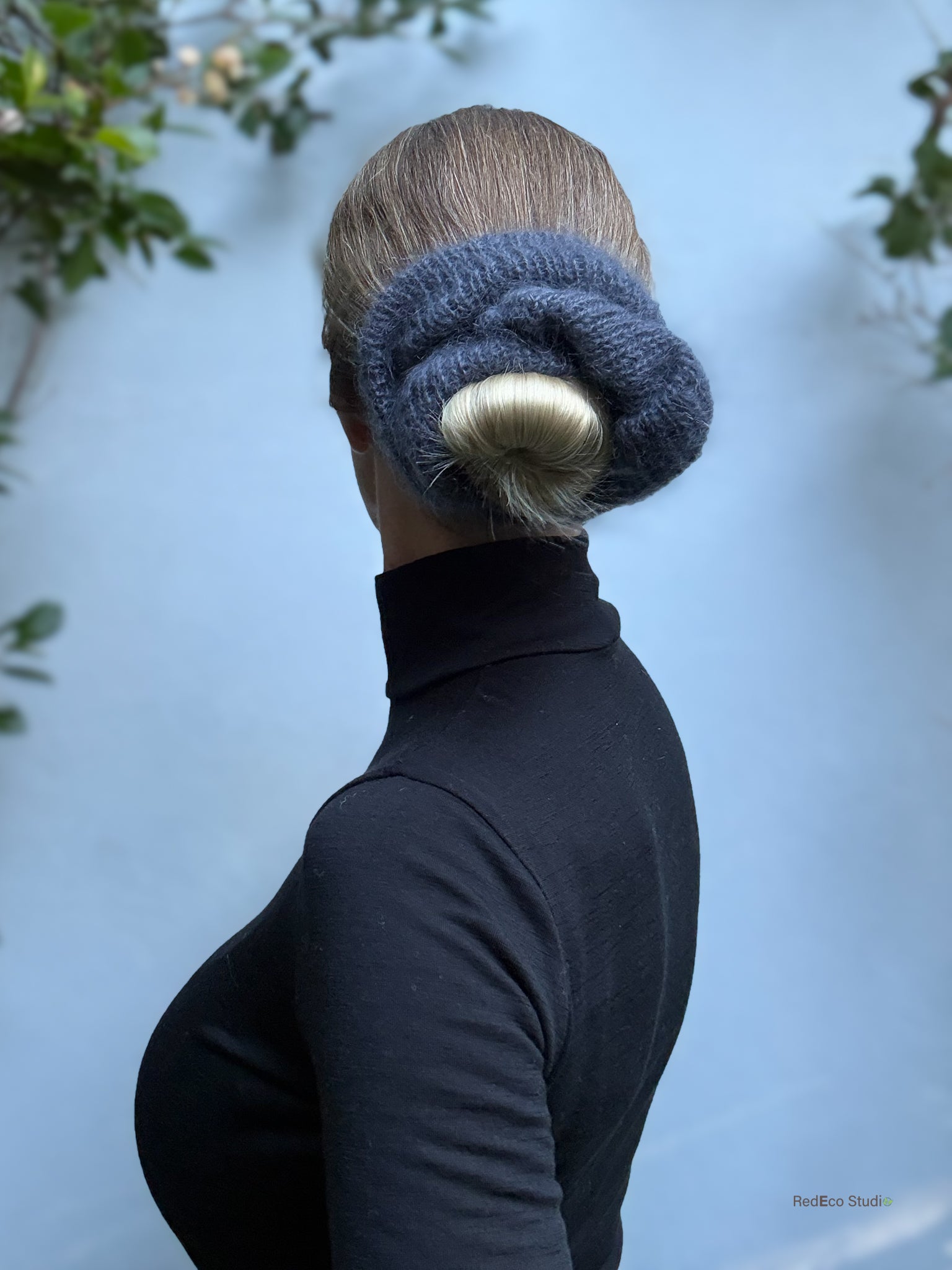Person wearing a grey knitted scrunchie with a bun against a light blue background