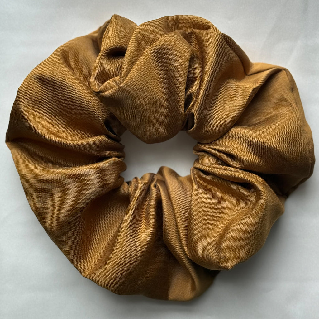 A very large silk twill scrunchie in a warm metallic gold or bronze shade, photographed flat against a light gray background.