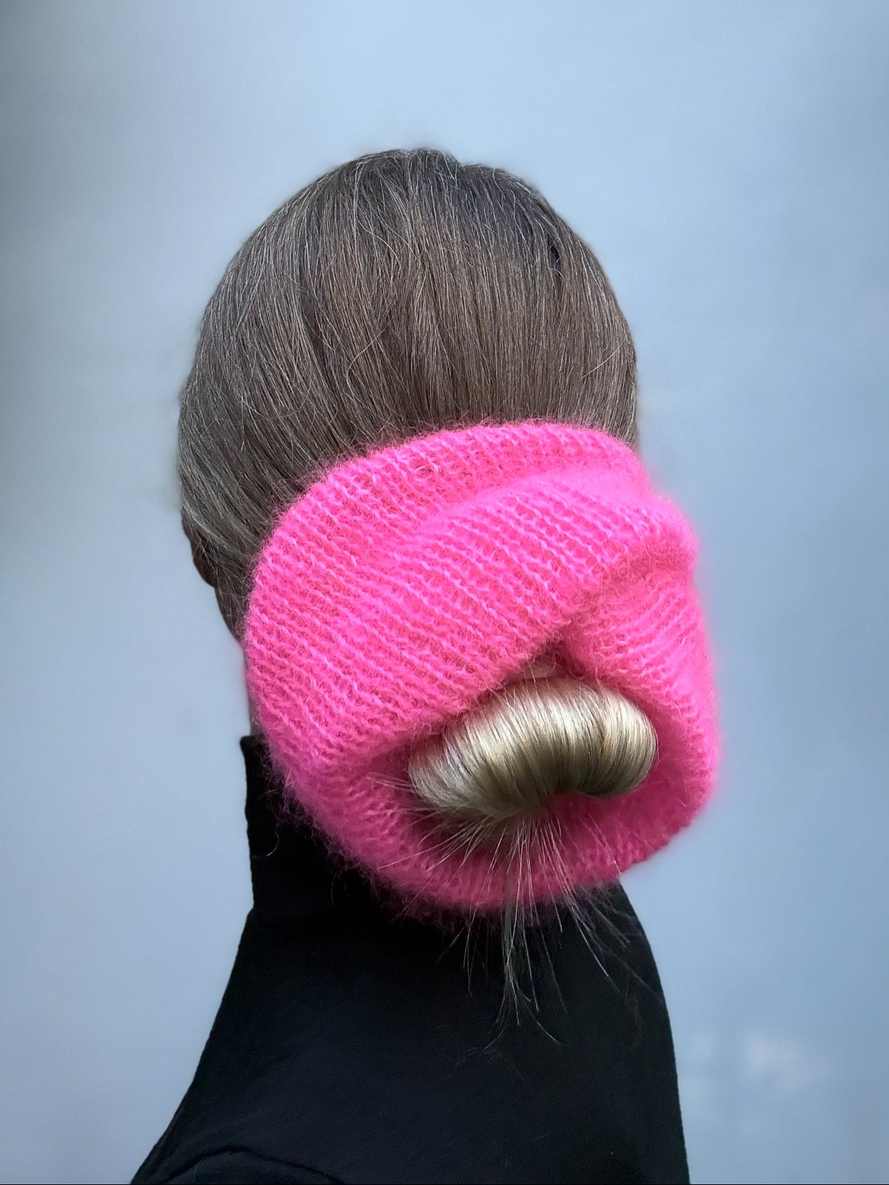 A bright pink knitted hair scrunchie worn around a person's hair, shown from the back against a soft gray background.
