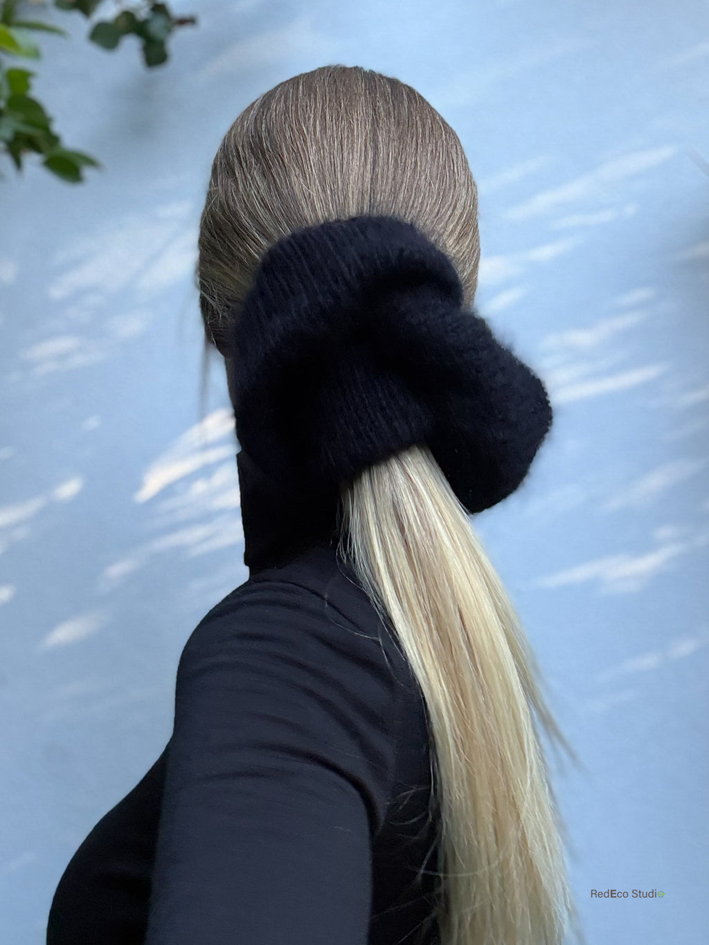 Person with a low ponytail wearing a black hand knitted scrunchie against a light blue background