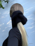 Person with a low ponytail wearing a black hand knitted scrunchie against a light blue background
