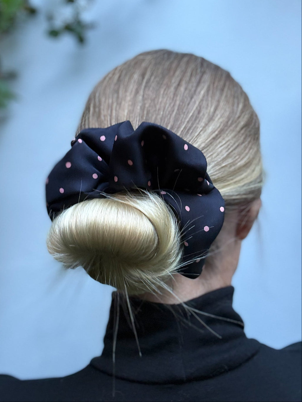 Person with a bun held up with a black polka dot scrunchie against a light blue background