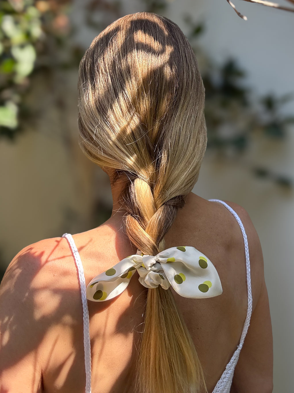 Person with braided hair tied with a polka dot silk bow scrunchie, outdoor setting