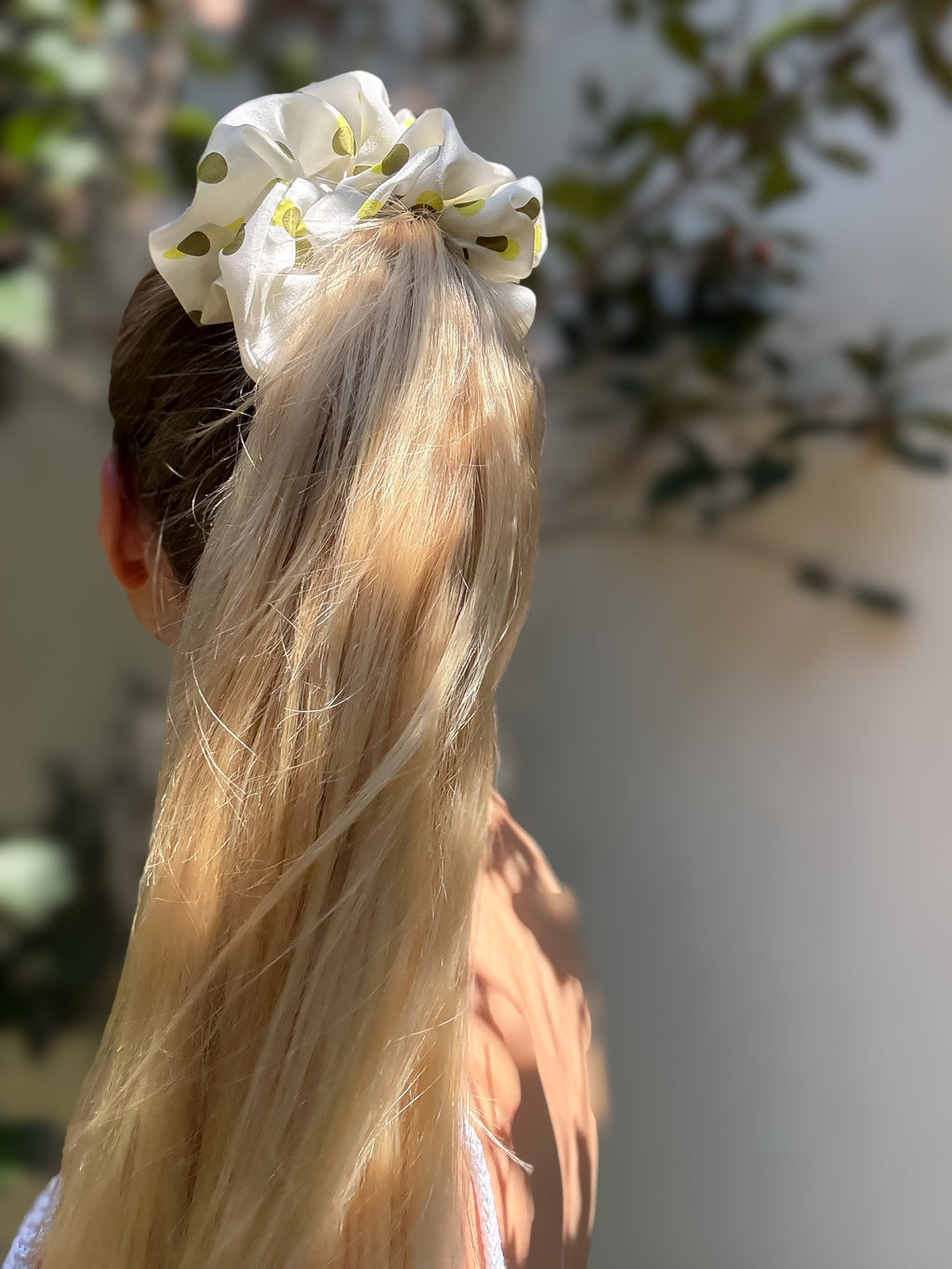Person with blonde hair tied with a white scrunchie against a blurred natural background
