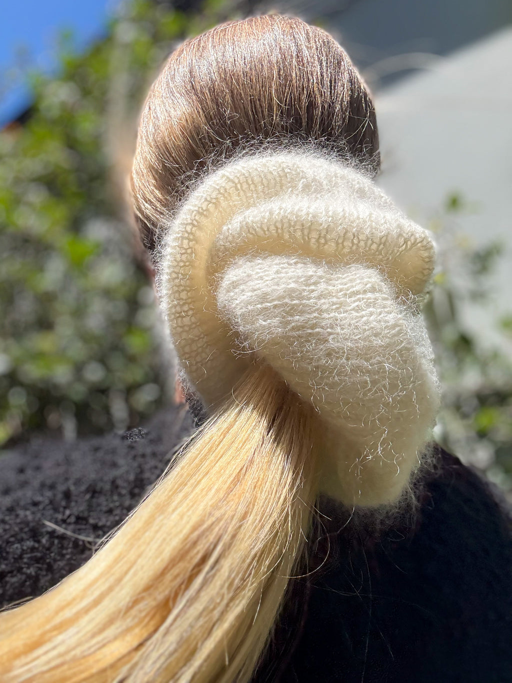 Close-up of an oversized extra large hand knitted hair scrunchie with blonde hair against a blurred natural background