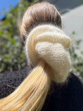 Close-up of an oversized extra large hand knitted hair scrunchie with blonde hair against a blurred natural background