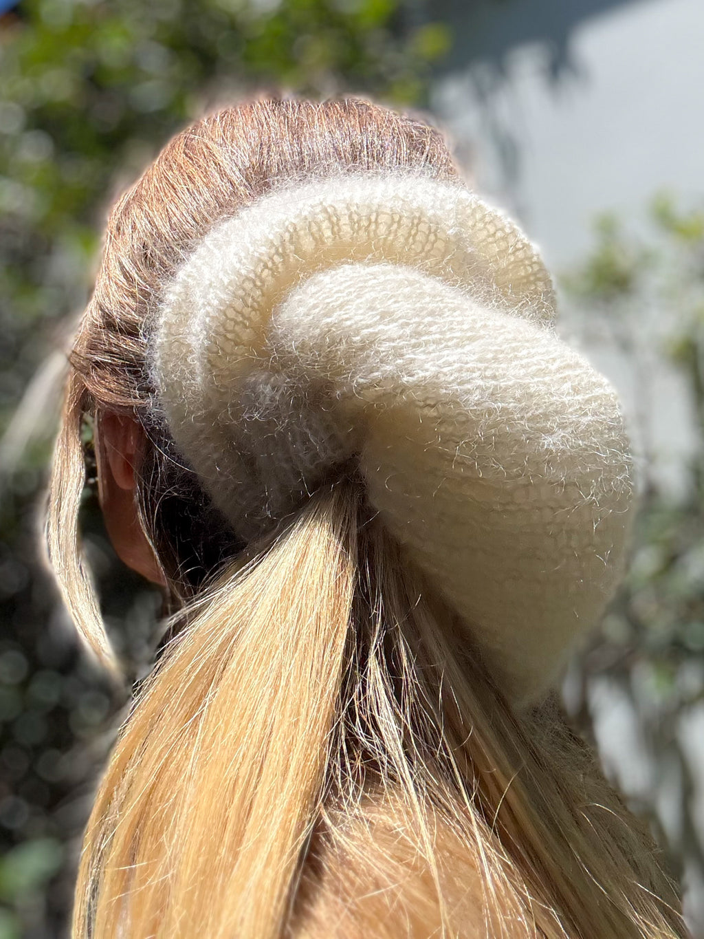 Close-up of a cream hand-knitted hair scrunchie on a ponytail with a blurred natural background