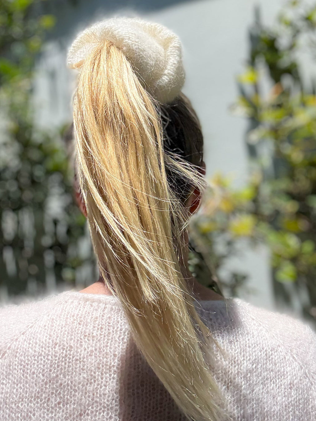 Person with long blonde hair tied in a high ponytail wearing a cream hand-knitted hair scrunchie