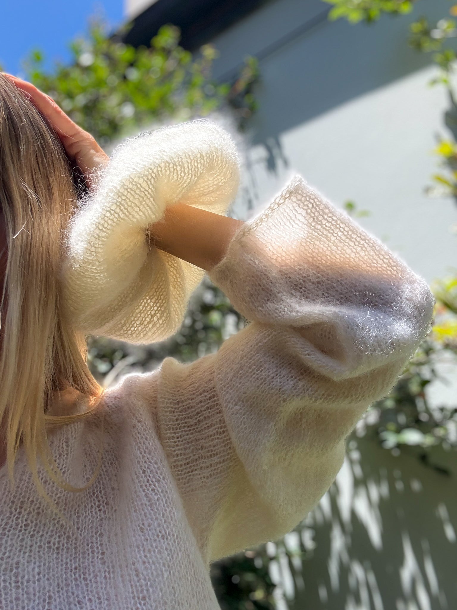Person holding a cream hand-knitted hair scrunchie with a blurred outdoor background
