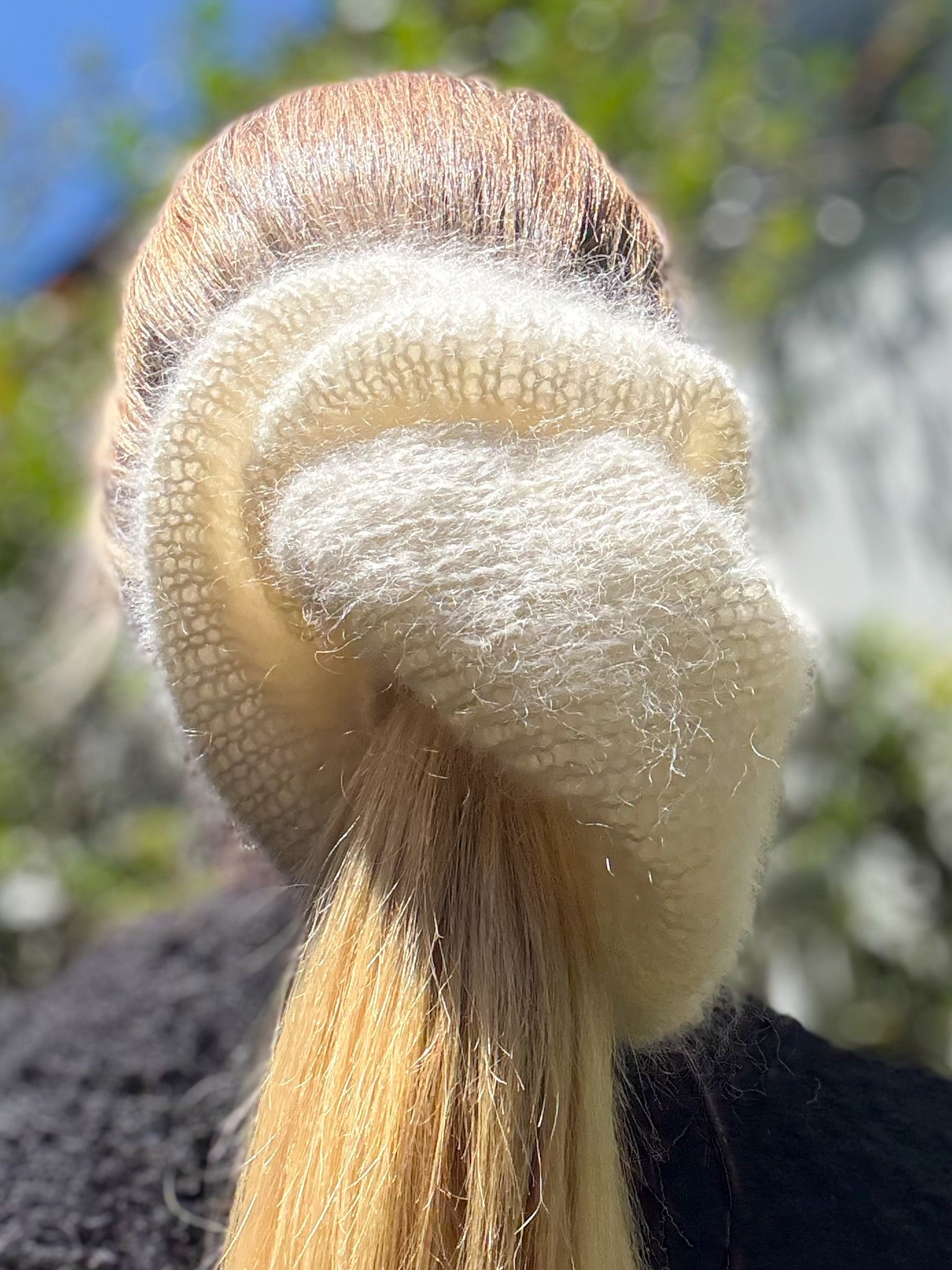 Close-up of a cream hand-knitted hair scrunchie wrapped around a low ponytail