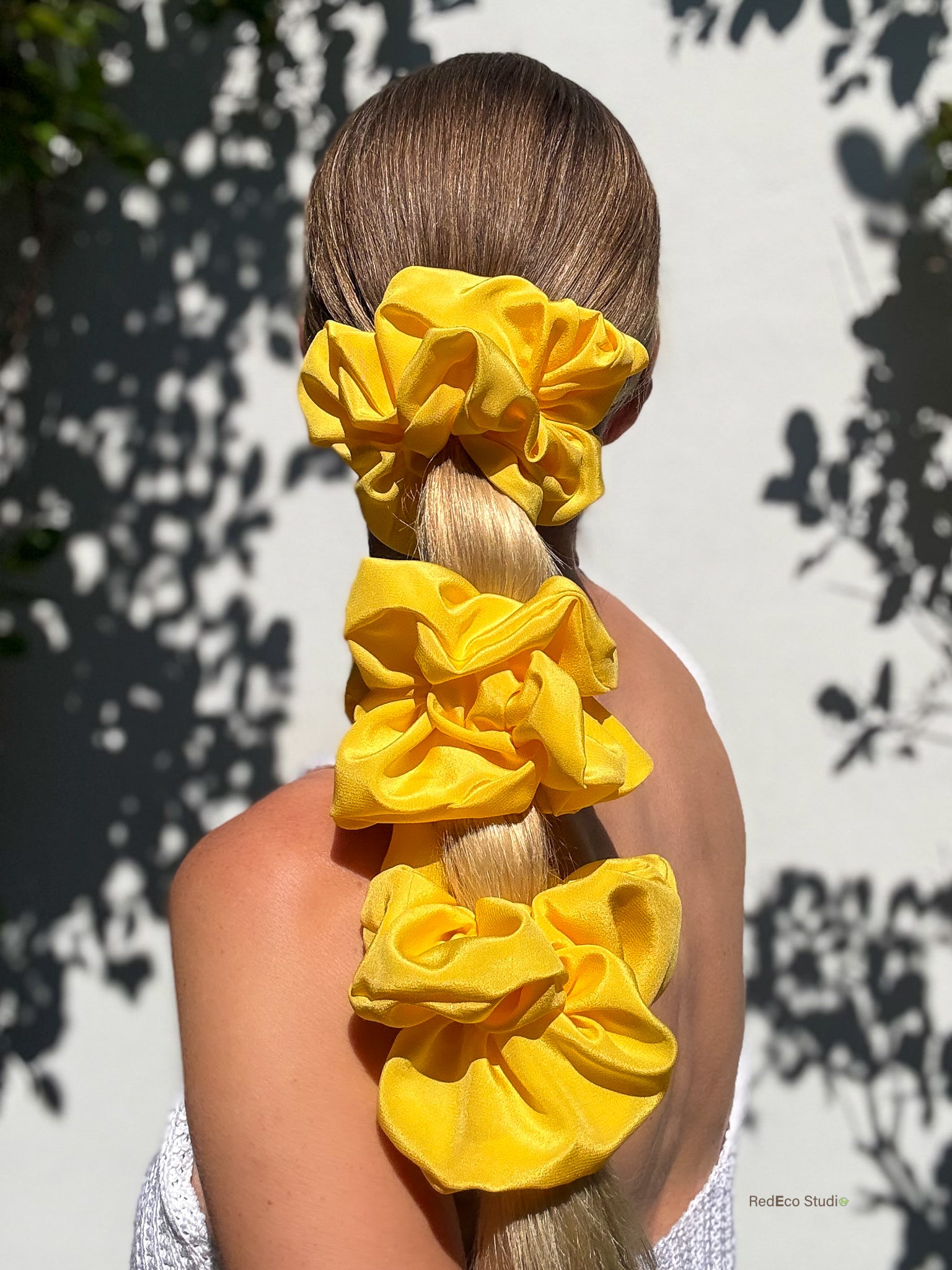 Person with long hair tied up with 3 large yellow scrunchies against a light background