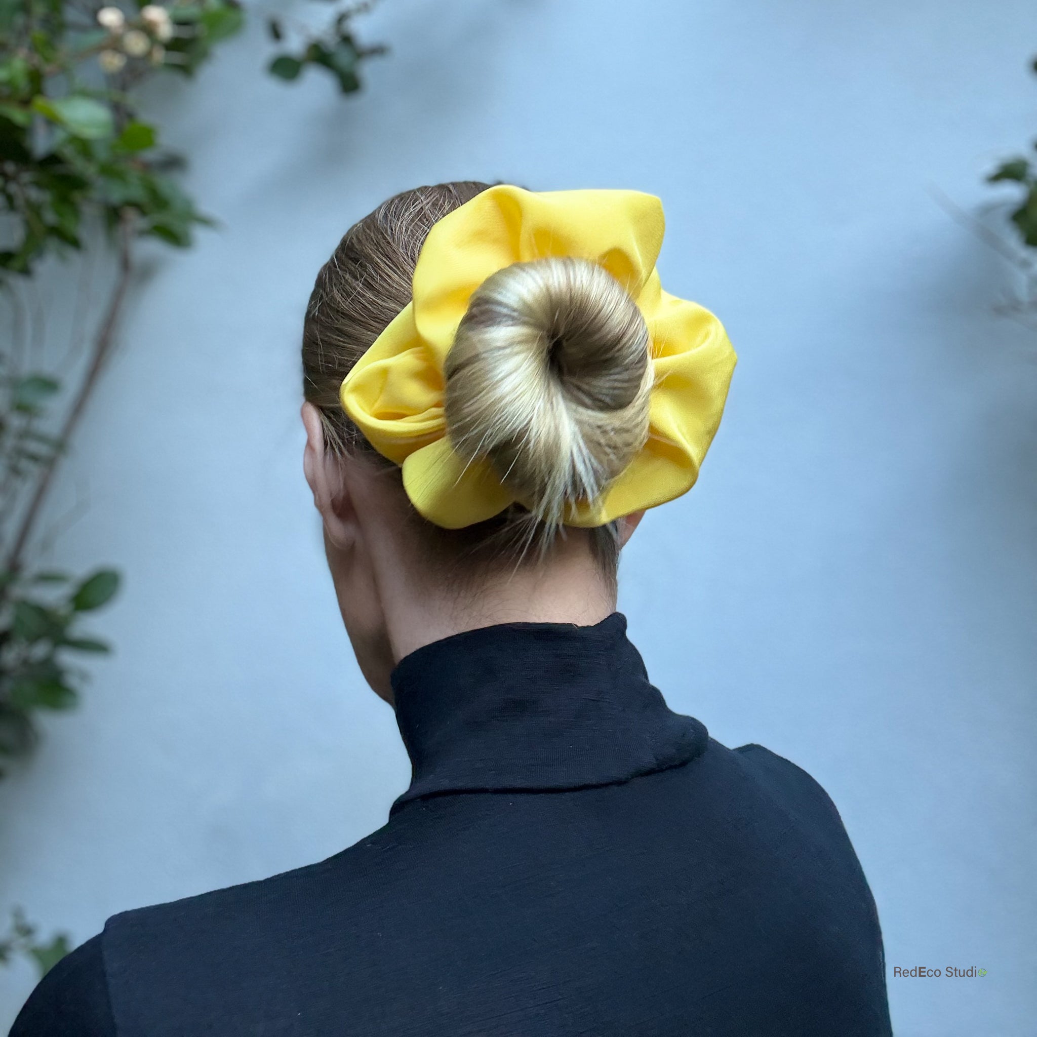 Person wearing a large yellow silk scrunchie in their hair against a light blue background