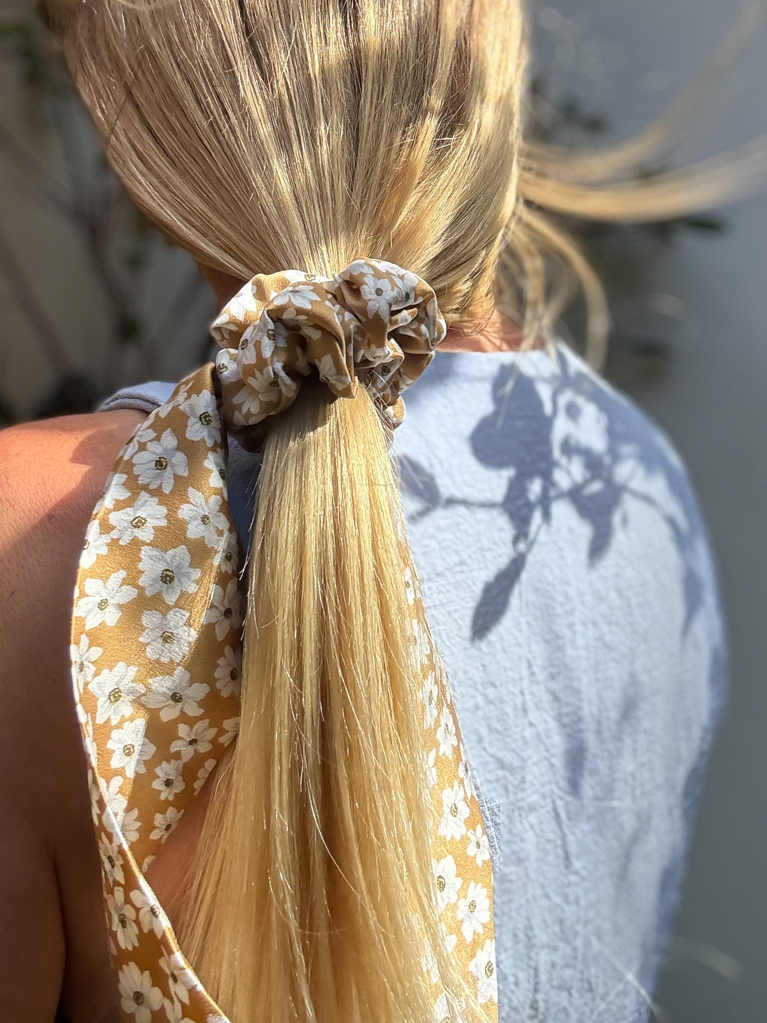 Close-up of a blonde ponytail with a floral classic silk scrunchie with tails, blurred background