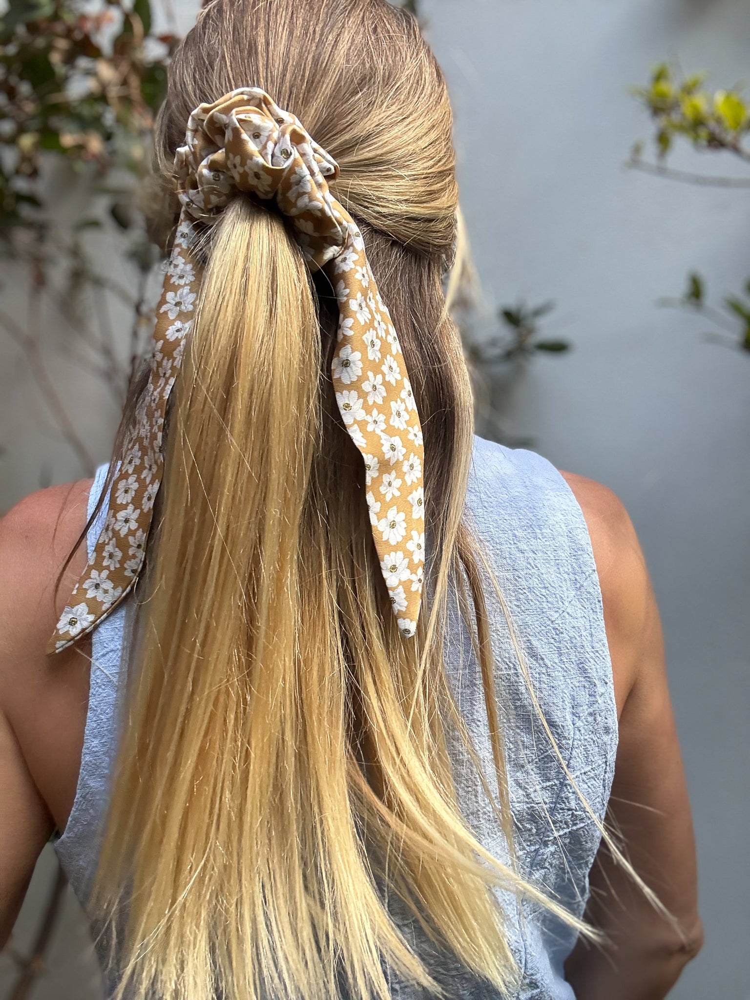 Person with long blonde hair tied back with a silk tail scrunchie against a blurred natural background