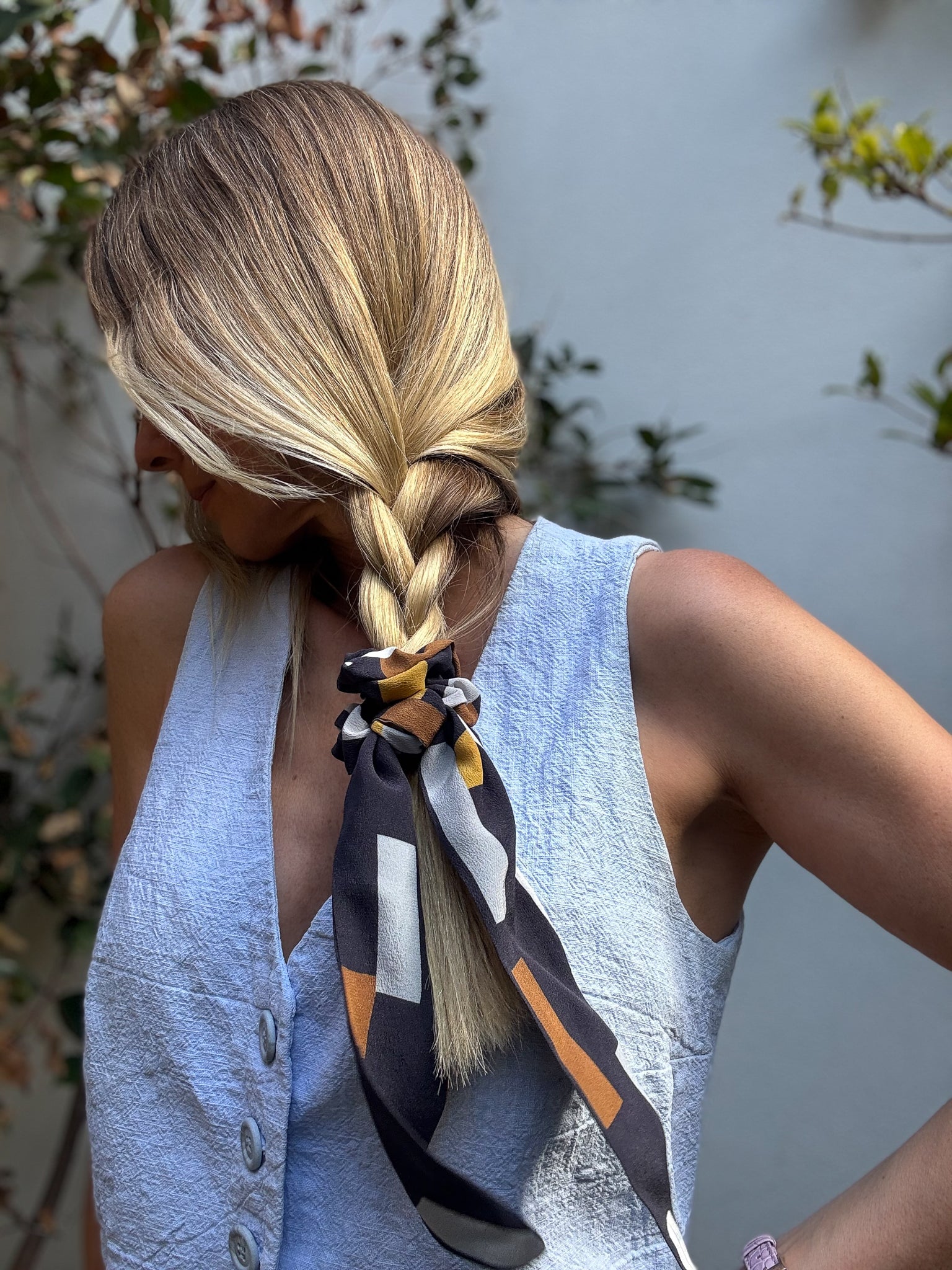 Person with styled hair using a colorful silk scrunchie against a blurred natural background