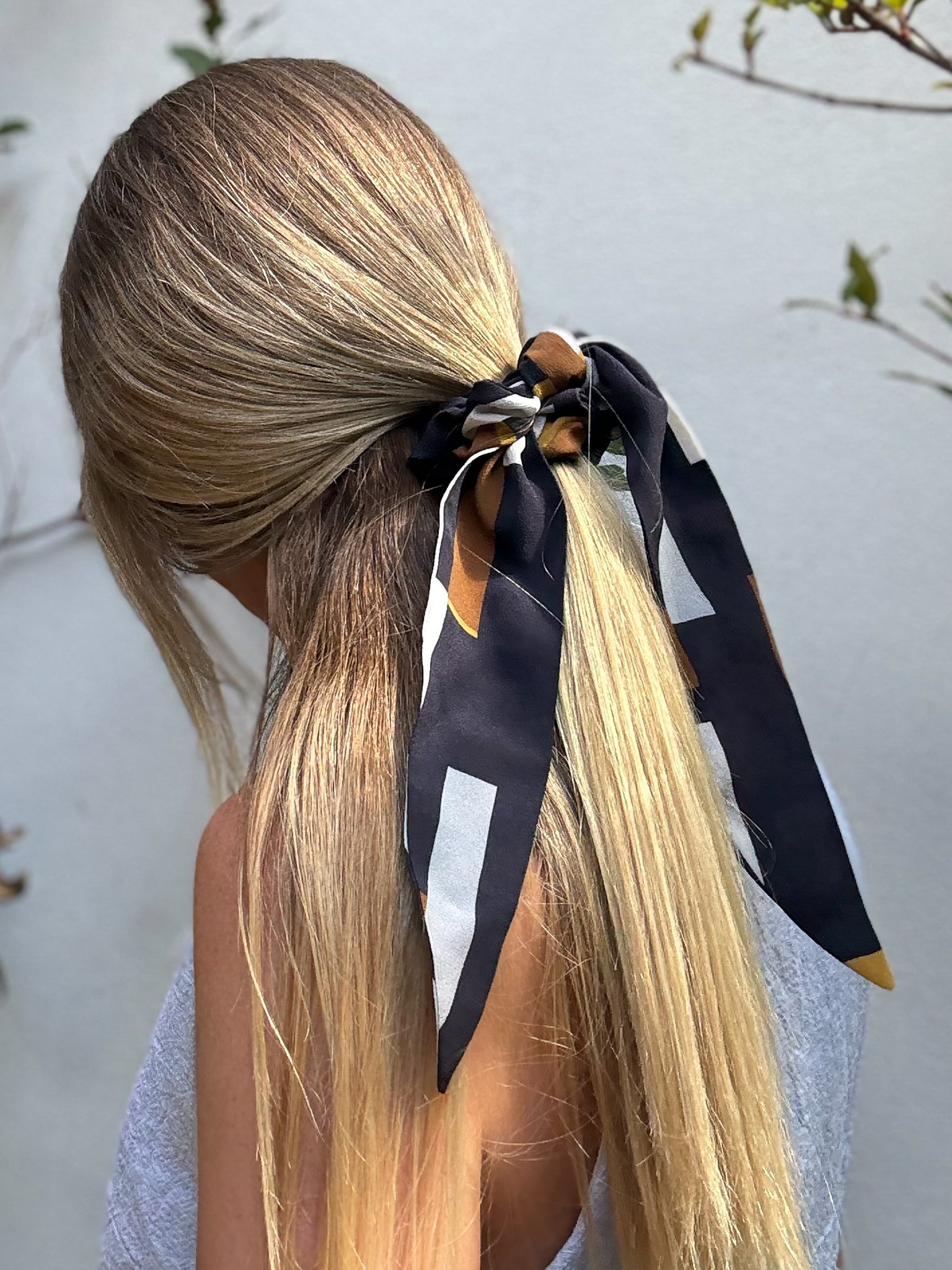 Blonde hair tied in a half ponytail with a silk scrunchie  against a neutral background