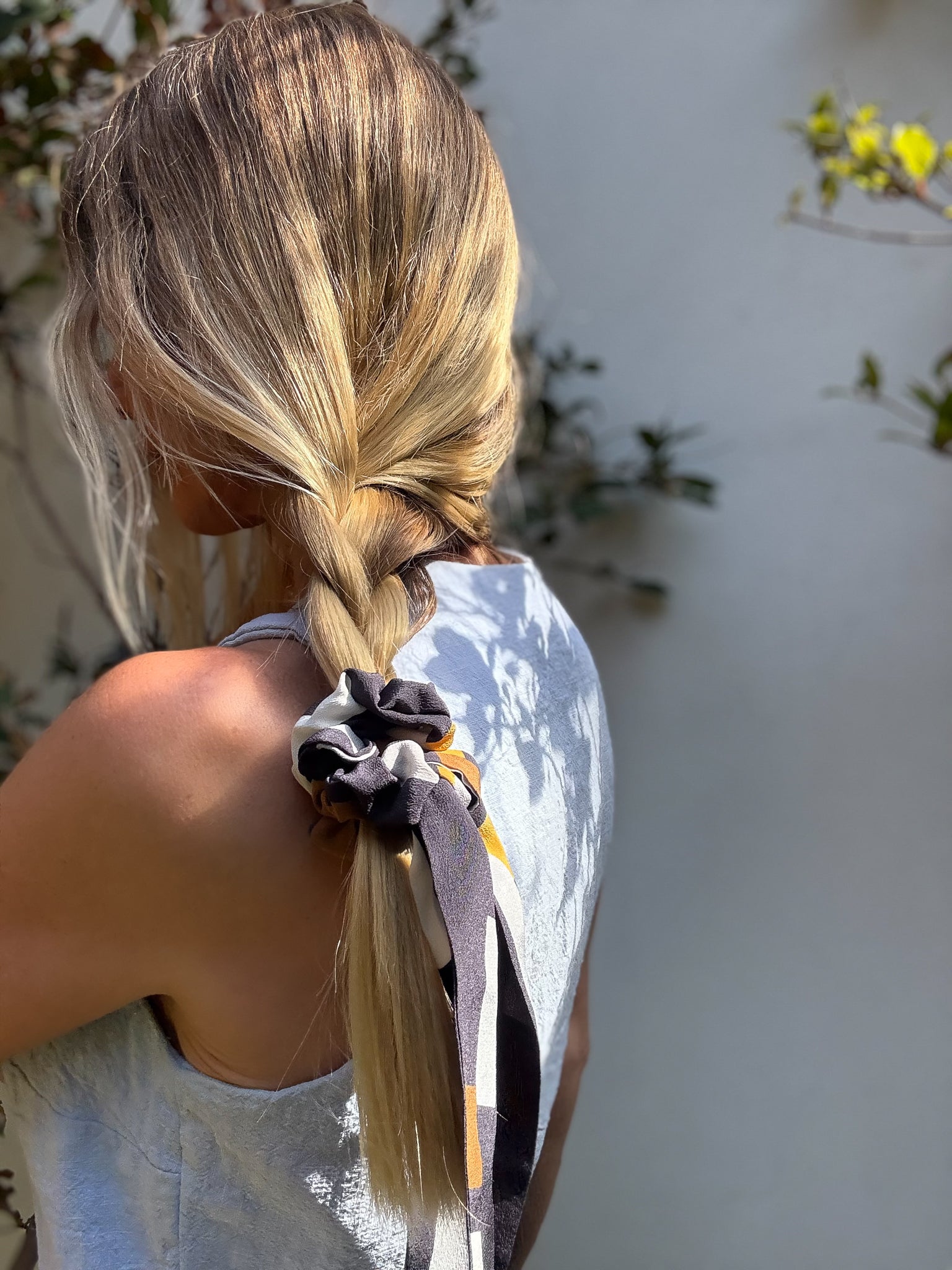 Person with a braid and silk tail scrunchie, standing outdoors with a blurred background