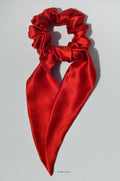 Red satin hair scrunchie with a bow on a light gray background