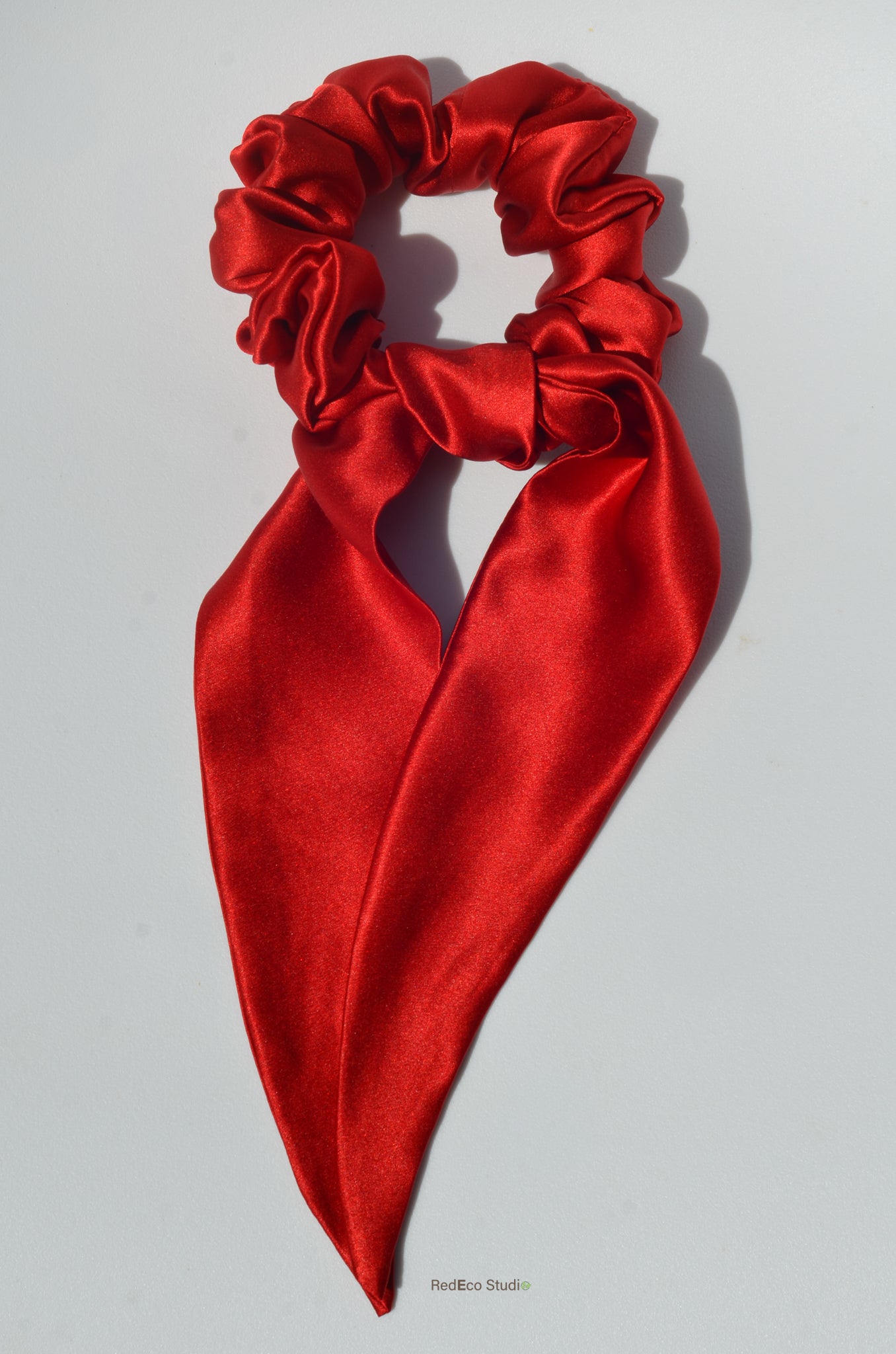 Red satin hair scrunchie with a bow on a light gray background