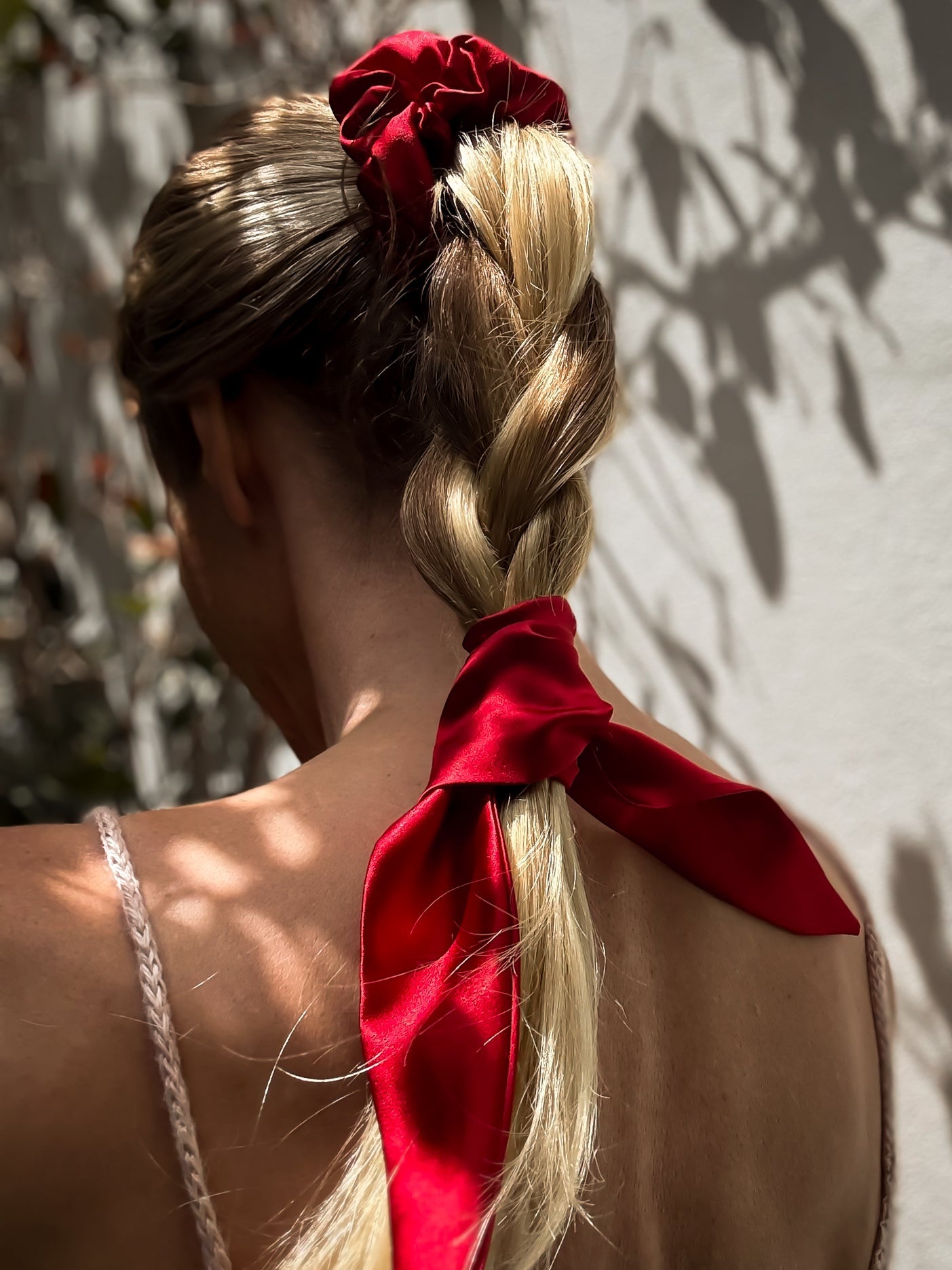 Person with braided hair tied with a red ribbon against a neutral background