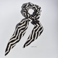 Black and white striped silk scrunchie with long tails on a light gray background