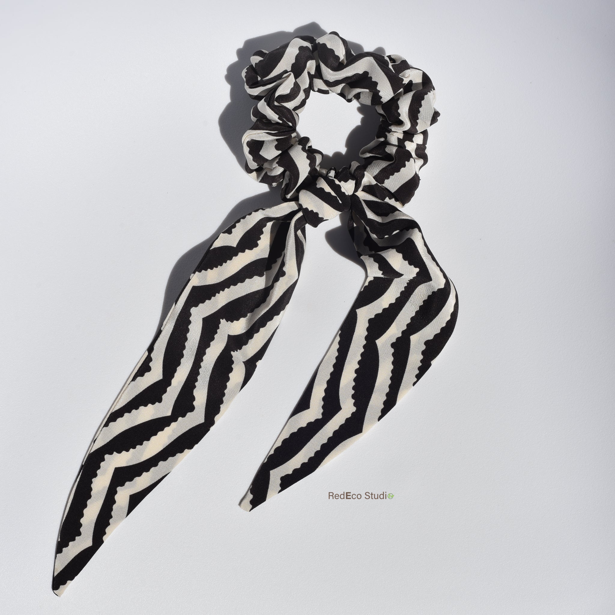 Black and white striped silk scrunchie with long tails on a light gray background