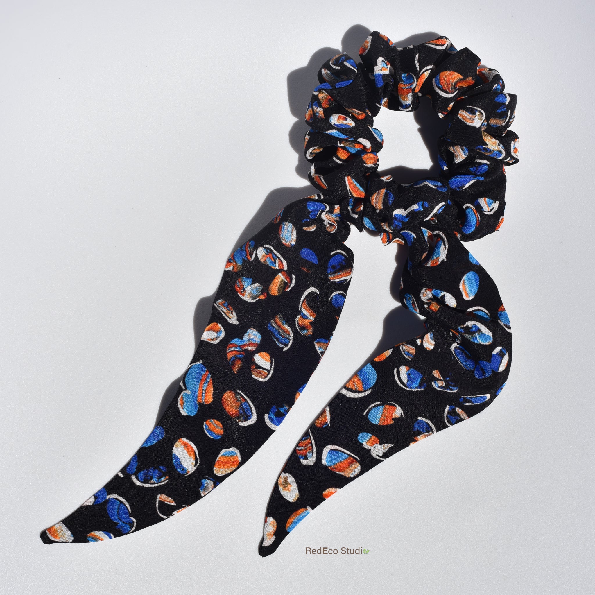 Silk scrunchie with long tails and colorful abstract pattern on a white background