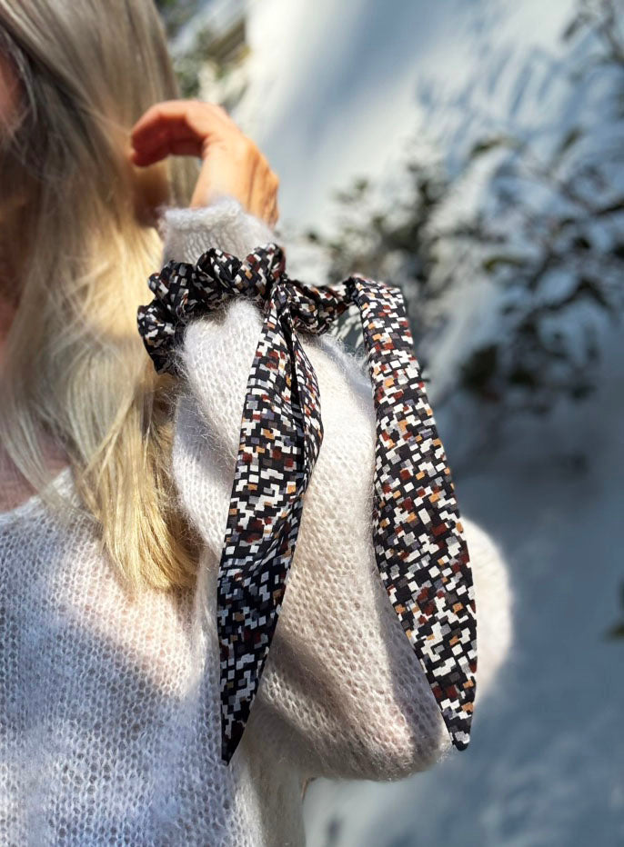 Person wearing a patterned silk scrunchie around their wrist. 