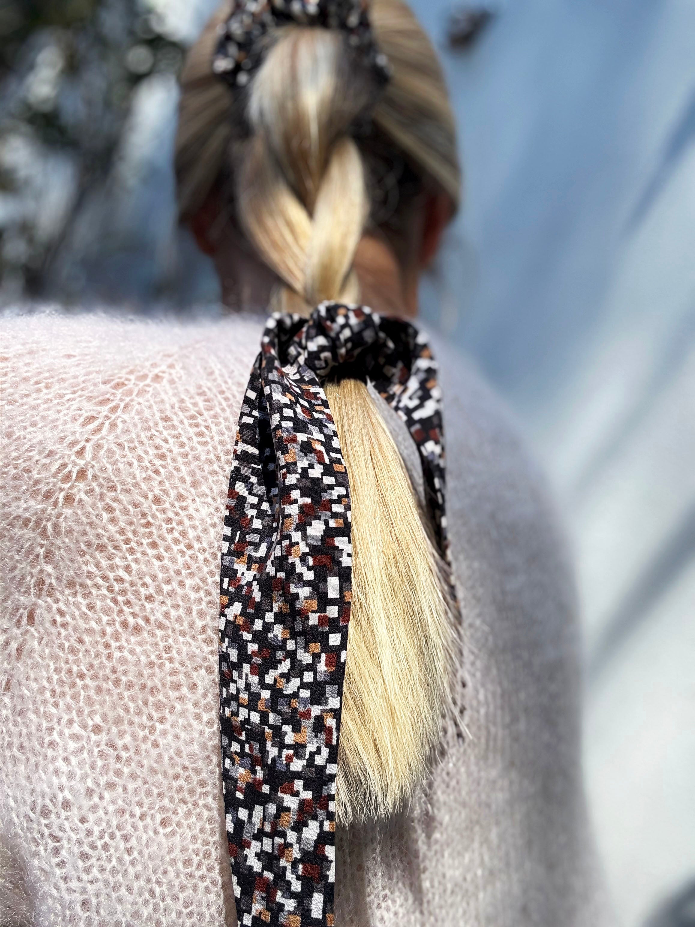 Close-up of a braided ponytail with a patterned silk scrunchie, blurred background