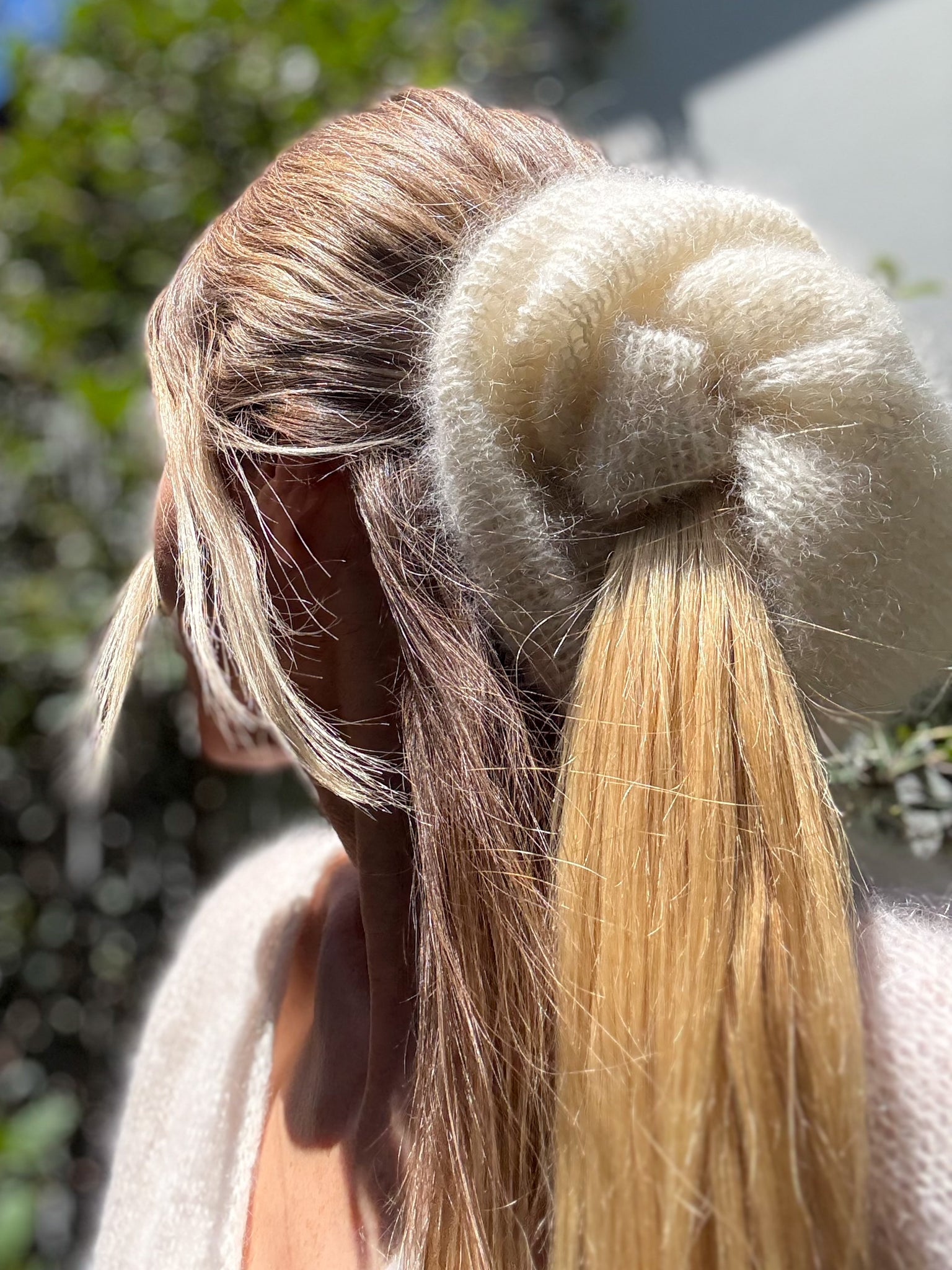 Close-up of a person with long blonde hair tied in a bun with a large beige hand knitted scrunchie 