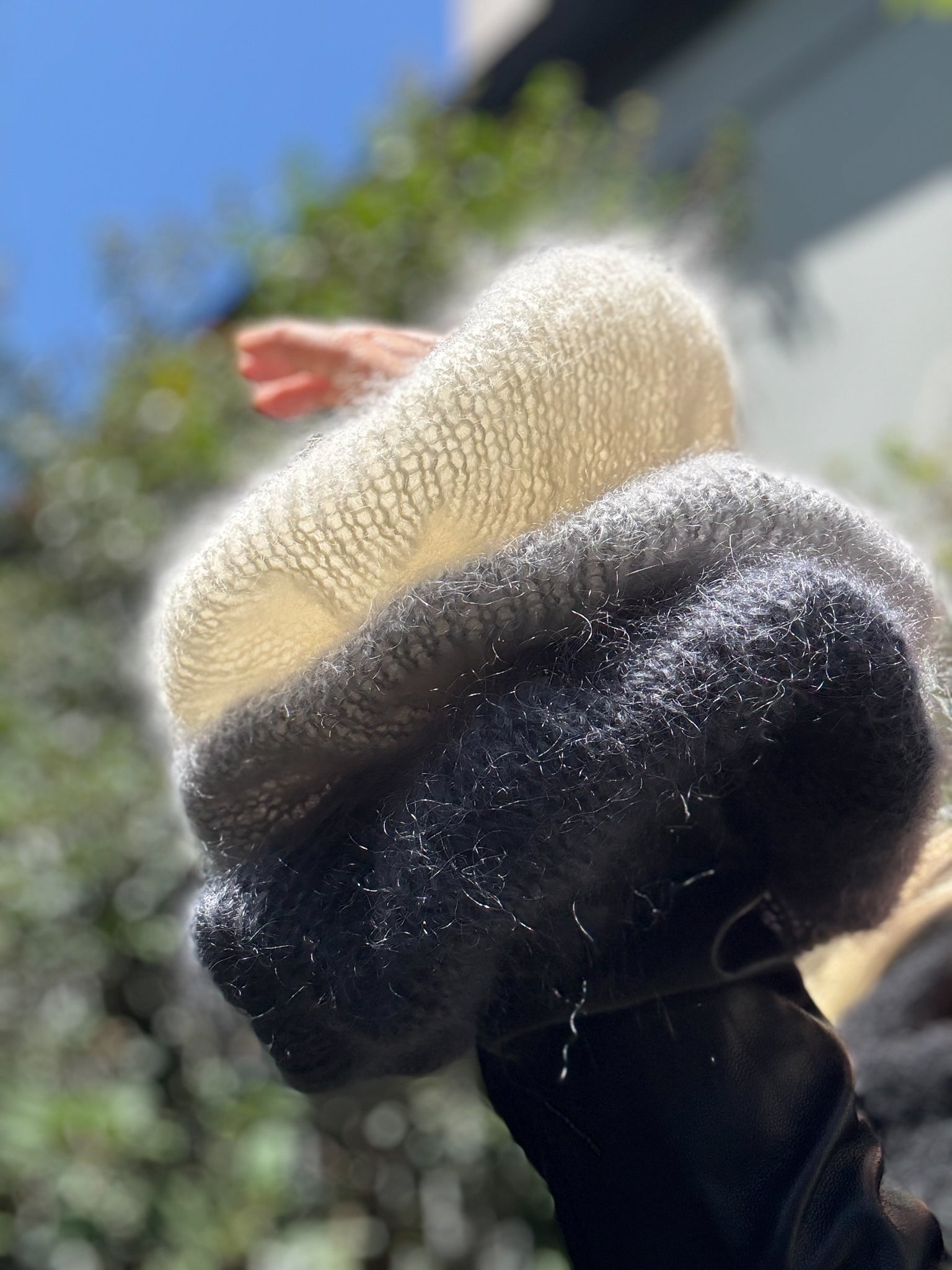 Close-up of 3 large hand knitted scrunchies against a blurred outdoor background.