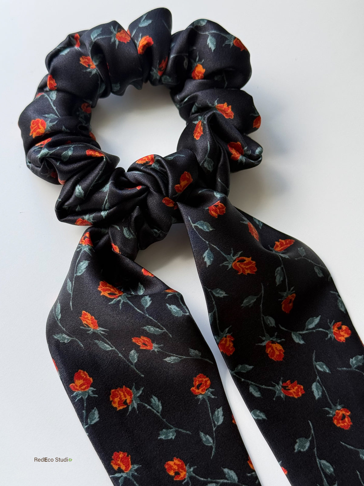 Close-up of the Ember Rose silk scarf scrunchie, showing the knot, glossy black satin and orange rosebuds on the tails