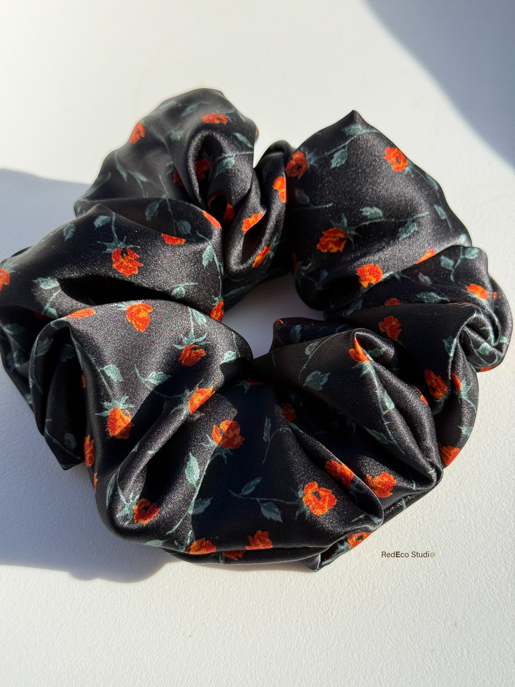 Close-up of the glossy silk satin and orange rosebud print on the Ember Rose scrunchie