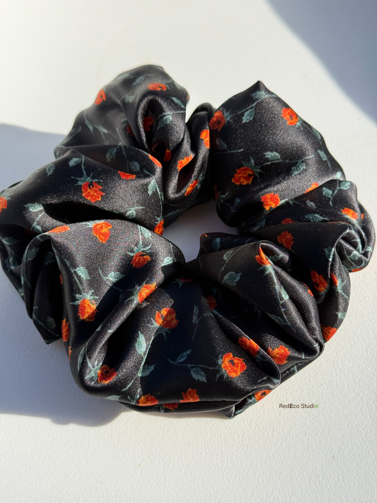 Close-up of the glossy silk satin and orange rosebud print on the Ember Rose scrunchie