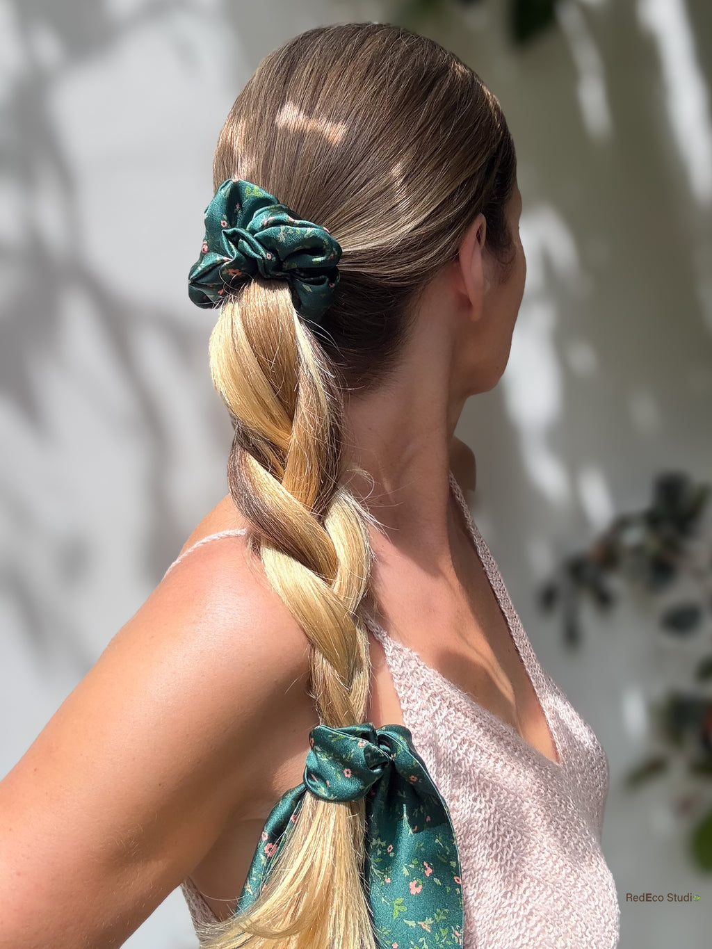 Emerald Posy silk scarf scrunchie on a braided ponytail, tail tied at the end, side view with a pink knit top