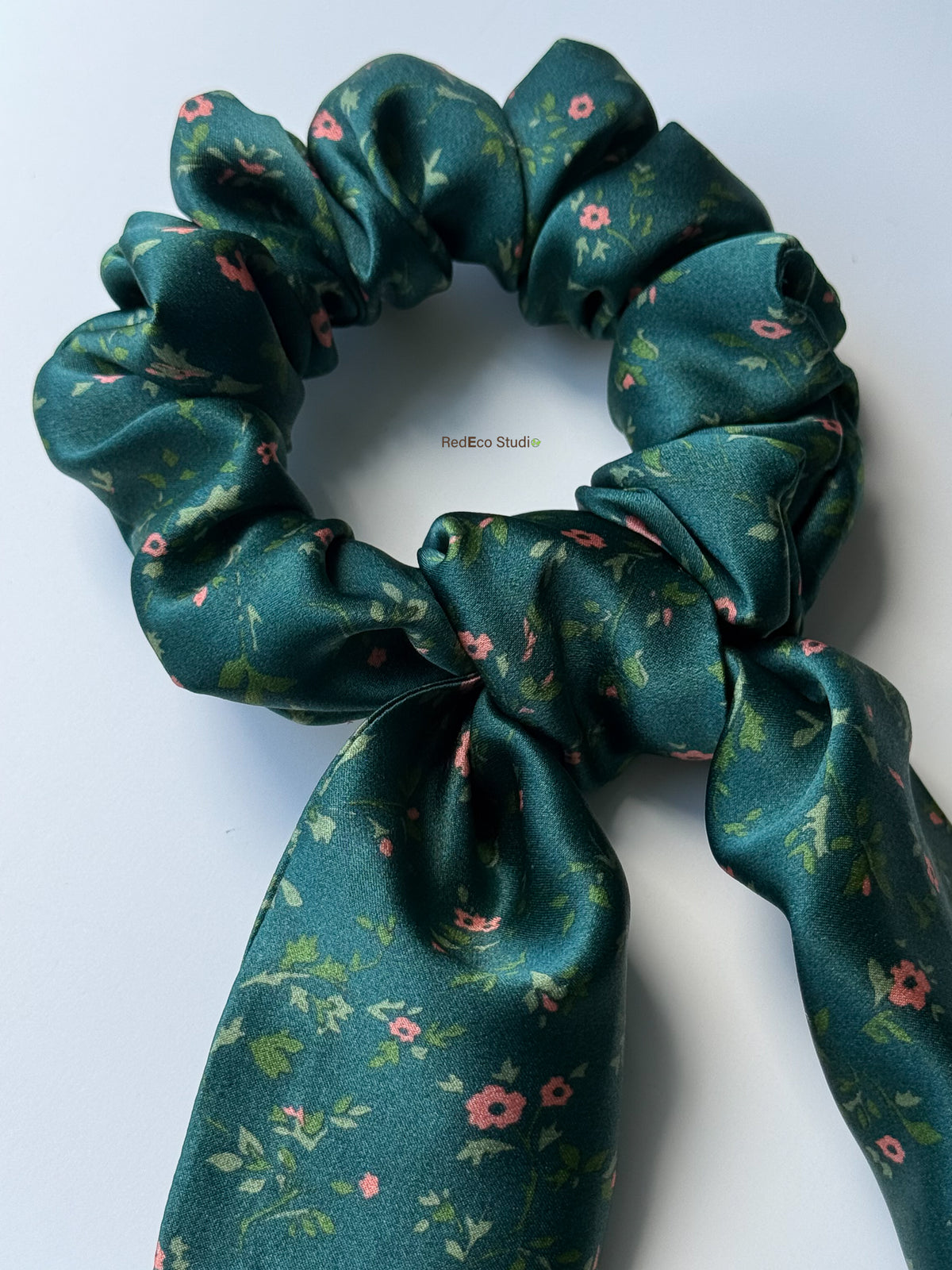 Close-up of the Emerald Posy silk scarf scrunchie, showing the knot, satin sheen and coral flowers on the tails
