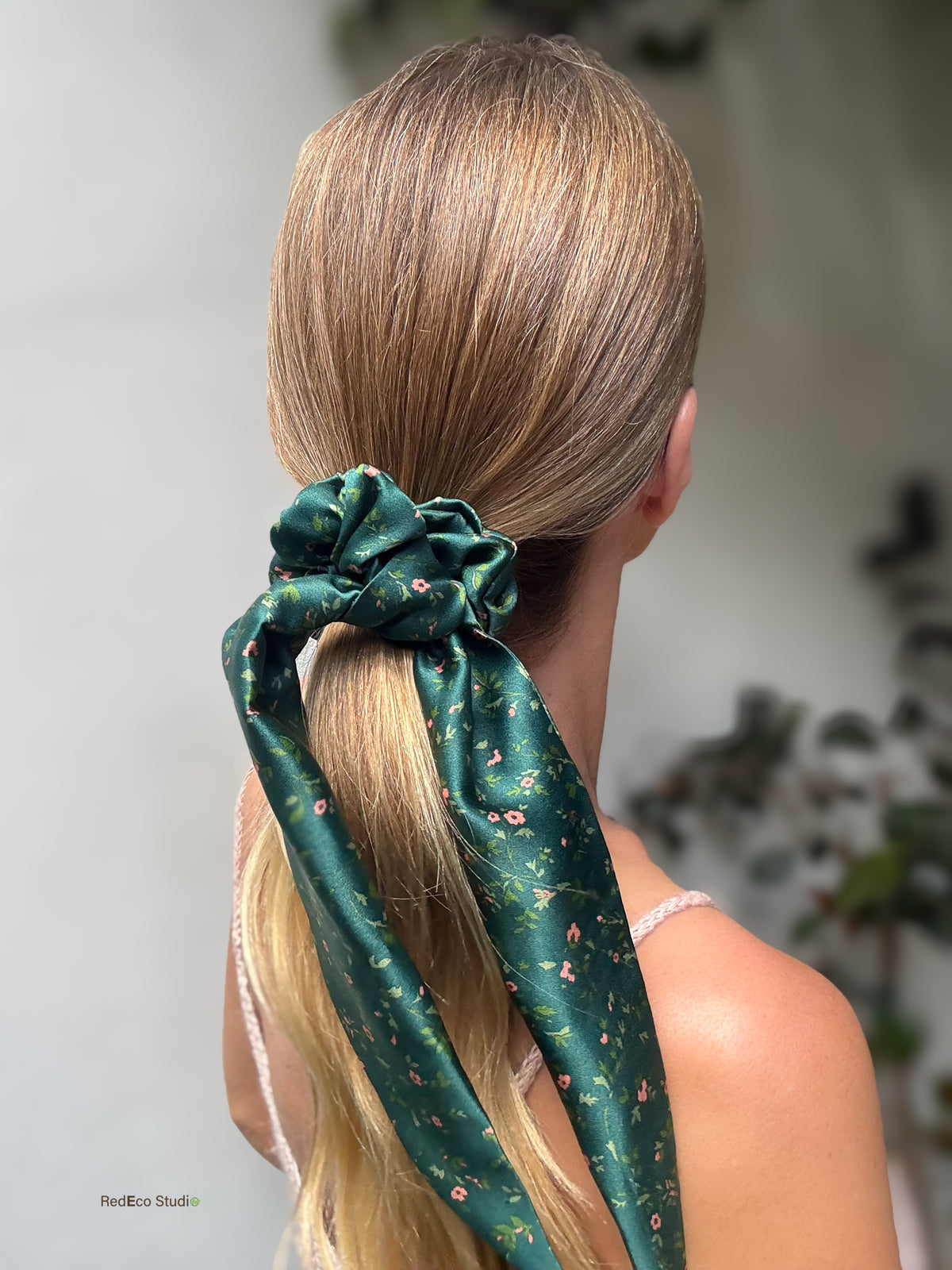 Emerald Posy silk scarf scrunchie on a sleek low ponytail, with its long floral tails trailing down, back view