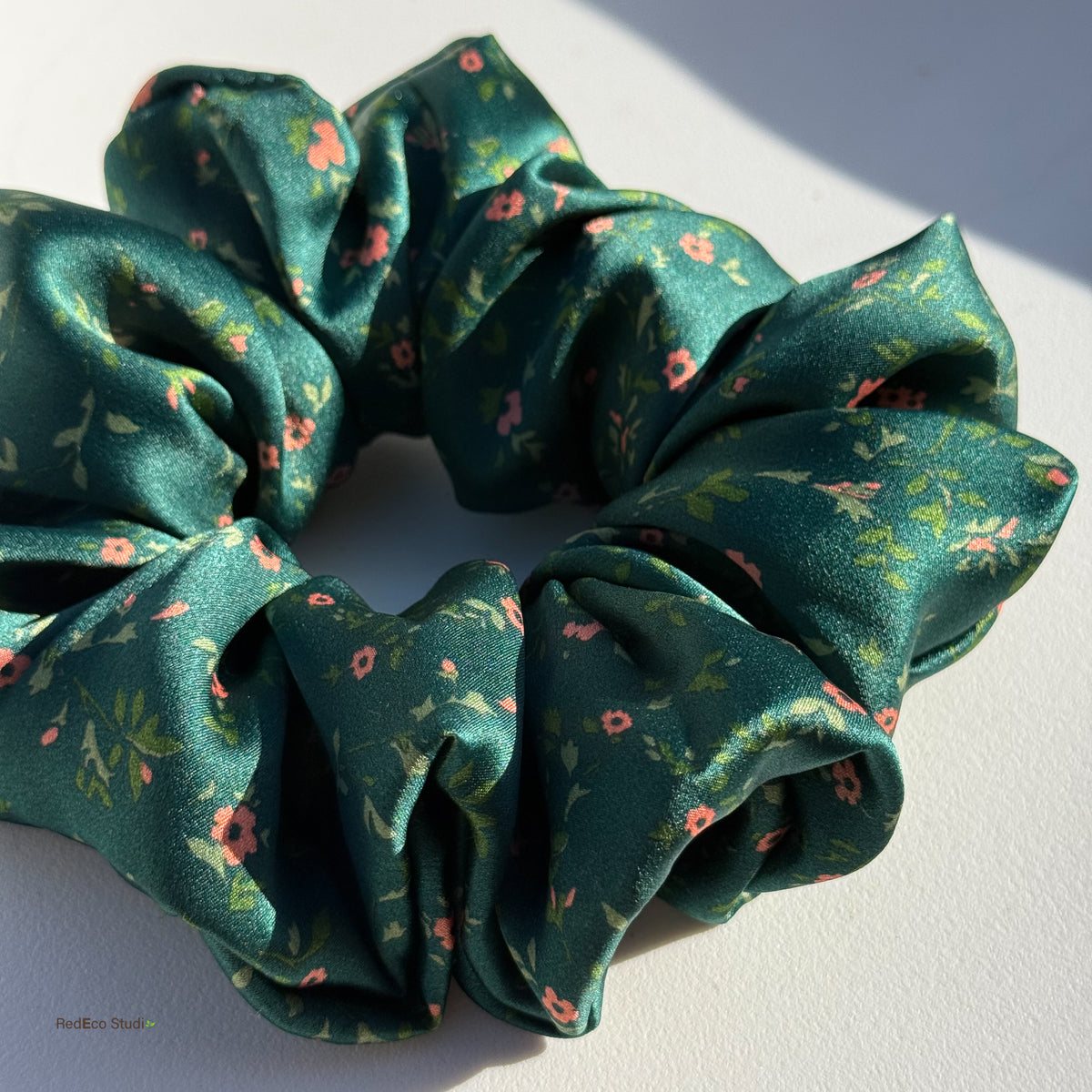 Close-up of the Emerald Posy oversized silk satin scrunchie in sunlight, showing its sheen and coral flowers on emerald green