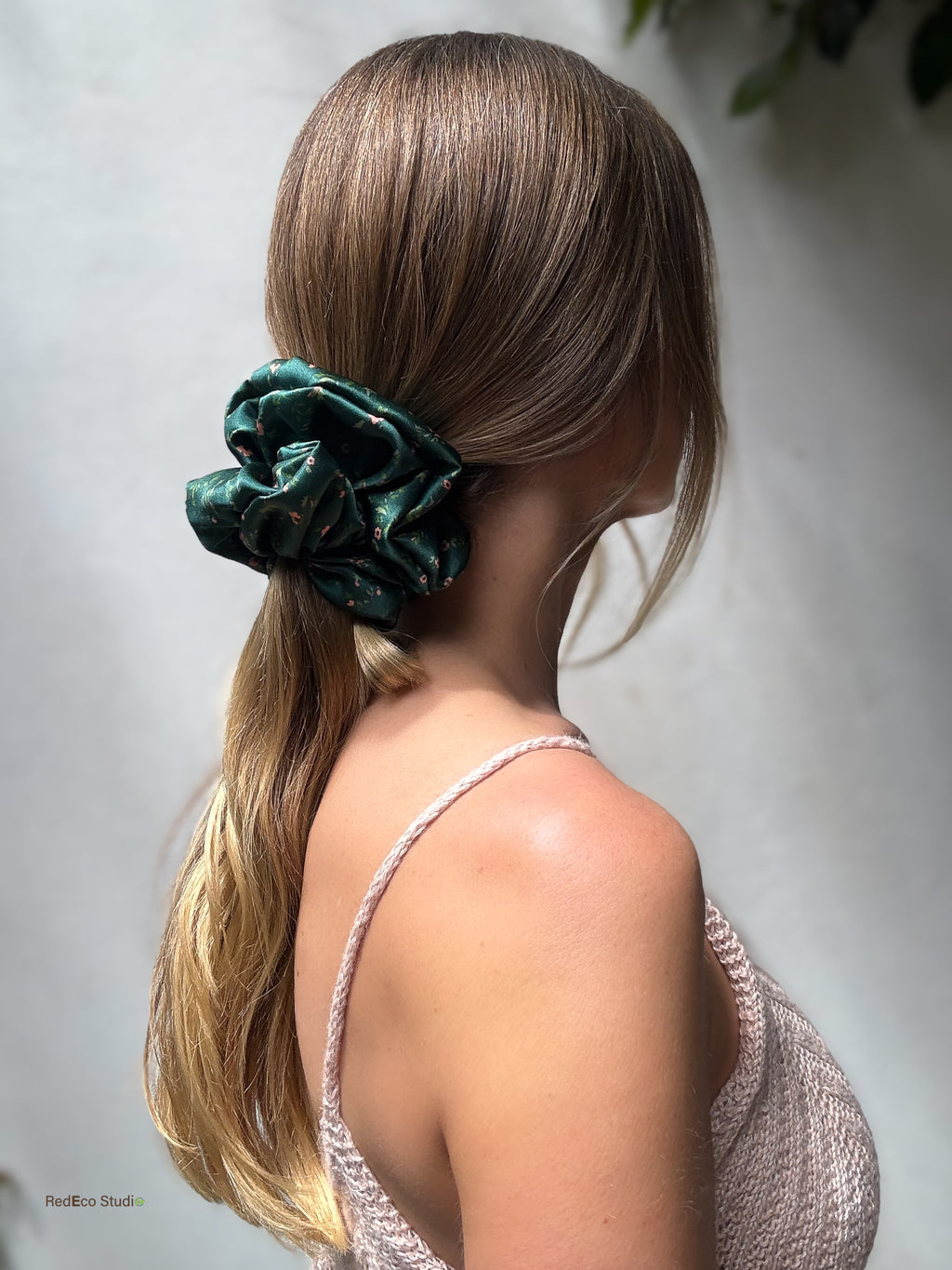 Side profile of a long low ponytail tied with the Emerald Posy oversized silk scrunchie, styled with a pink knit top