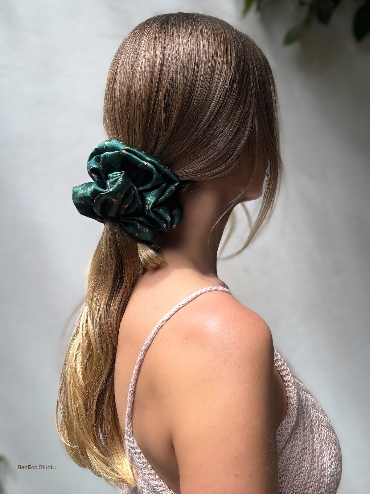 Side profile of a long low ponytail tied with the Emerald Posy oversized silk scrunchie, styled with a pink knit top